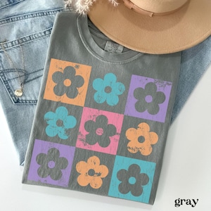 May include: A gray t-shirt with a pattern of colorful flowers. The flowers are in a grid pattern and have a distressed look. The shirt is made of a soft, comfortable material.