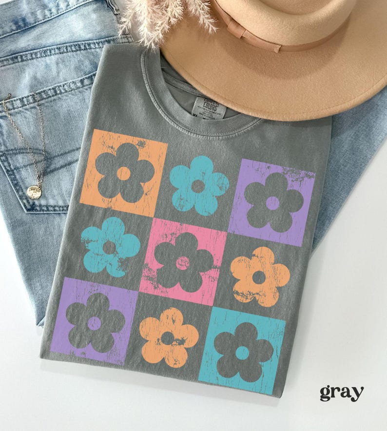 May include: A gray t-shirt with a pattern of colorful flowers. The flowers are in a grid pattern and have a distressed look. The shirt is made of a soft, comfortable material.