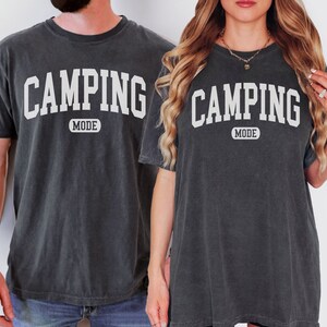 May include: Two black t-shirts with white text that reads "Camping Mode".
