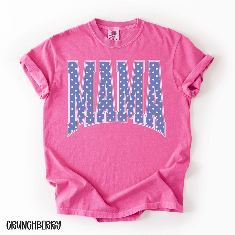 May include: A pink t-shirt with the word "MAMA" in large, blue letters with white polka dots. The shirt has rolled-up sleeves and the word "CRUNCHBERRY" is printed at the bottom.