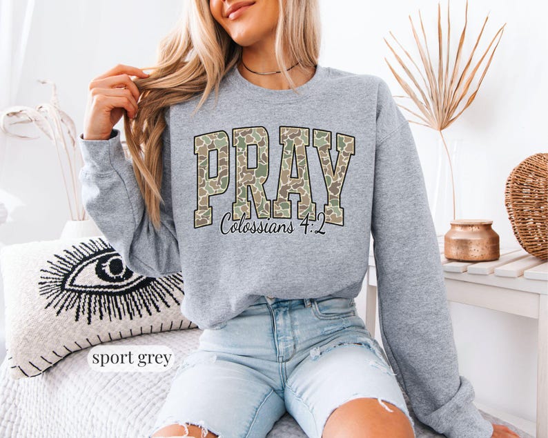 May include: Sport grey sweatshirt with the word "PRAY" in a camouflage pattern across the chest. The text "Colossians 4:2" is below the word "PRAY". The sweatshirt is a crew neck style.