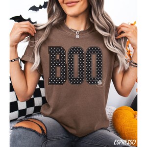 Puede incluir: Una camiseta marr&oacute;n de manga corta con la palabra BOO impresa en letras grandes de bloque. Las letras son negras con un patr&oacute;n de puntos blancos y un borde fino. La camiseta tiene cuello redondo y corte holgado, con la palabra ESPRESSO en la parte inferior.