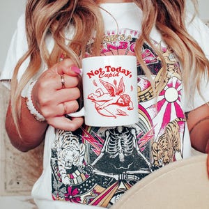 May include: White ceramic mug with a red graphic of a winged cupid with an arrow and the text "Not Today, Cupid".