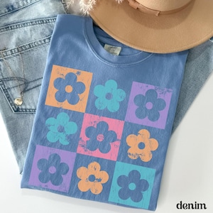May include: A blue t-shirt with a retro floral design. The flowers are in squares and are in shades of orange, pink, blue, and purple.