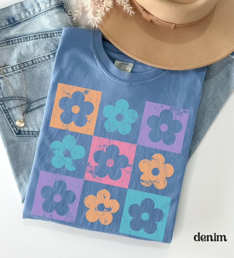May include: A blue t-shirt with a retro floral design. The flowers are in squares and are in shades of orange, pink, blue, and purple.