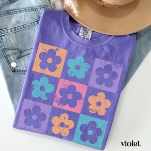 May include: A purple t-shirt with a pattern of colorful flowers in a grid design. The shirt has a tag that says "Comfy Colors" and "XL - 70 - 80".