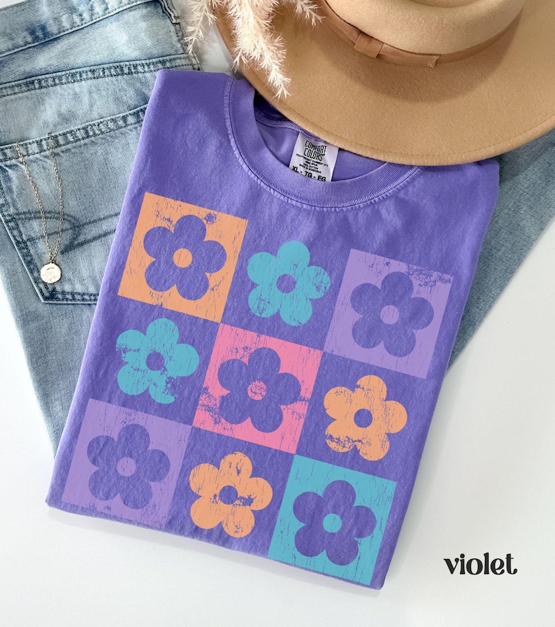 May include: A purple t-shirt with a pattern of colorful flowers in a grid design. The shirt has a tag that says "Comfy Colors" and "XL - 70 - 80".