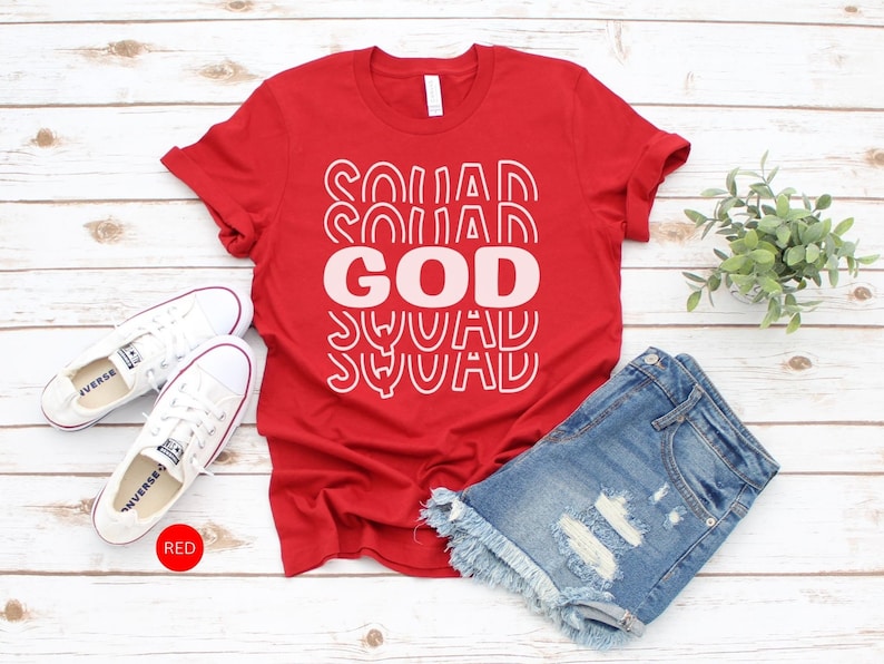 Pu&ograve; includere: Maglietta rossa con il testo "GOD SQUAD" in lettere bianche e rosa. La maglietta &egrave; abbinata a pantaloncini di jeans e scarpe da ginnastica bianche.