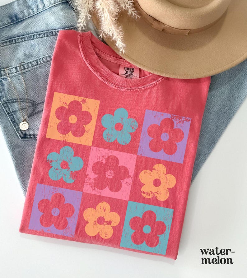 May include: A red t-shirt with a pattern of colorful flowers in squares. The flowers are in shades of pink, blue, orange, and yellow.