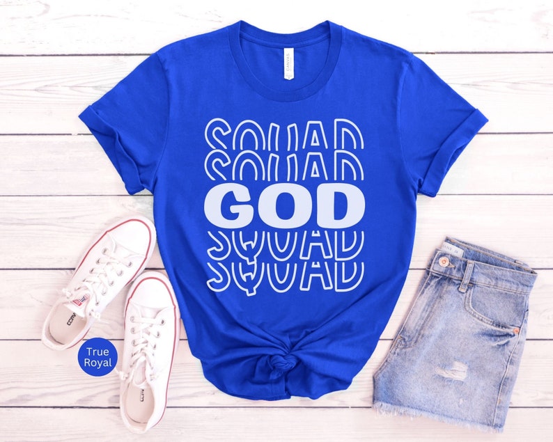 Pu&ograve; includere: Una maglietta blu reale con una grafica bianca che dice "God Squad" in un font retr&ograve;.