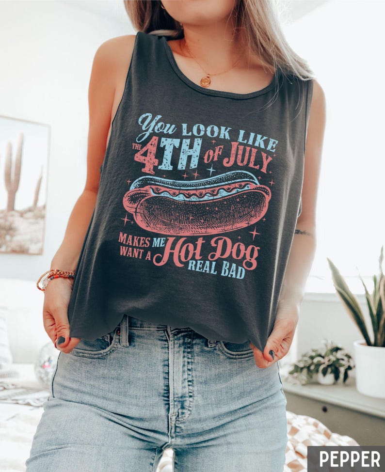Puede incluir: Camiseta sin mangas gris oscuro con un gr&aacute;fico de un perrito caliente y el texto "You look like the 4th of July makes me want a hot dog real bad." La camiseta sin mangas se usa con jeans azules.