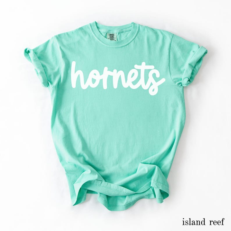 May include: A light turquoise t-shirt with the word "hornets" in white script across the front. The shirt is made of soft material and has rolled-up sleeves. The color is labeled "island reef".