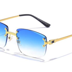 Puede incluir: Gafas de sol con montura dorada y lentes azules degradados. La montura es de forma cuadrada con un dise&ntilde;o delgado y elegante.