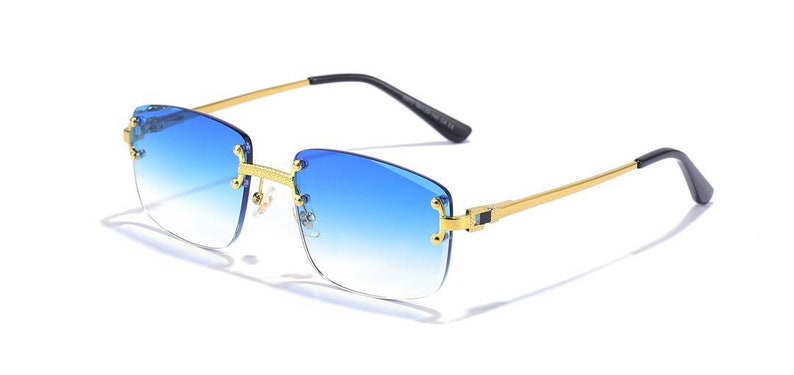 Puede incluir: Gafas de sol con montura dorada y lentes azules degradados. La montura es de forma cuadrada con un dise&ntilde;o delgado y elegante.
