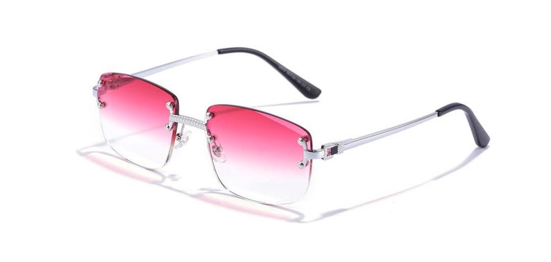 Puede incluir: Gafas de sol con montura plateada y lentes de color rosa degradado. Las gafas tienen un dise&ntilde;o sin montura y una fina montura de metal.