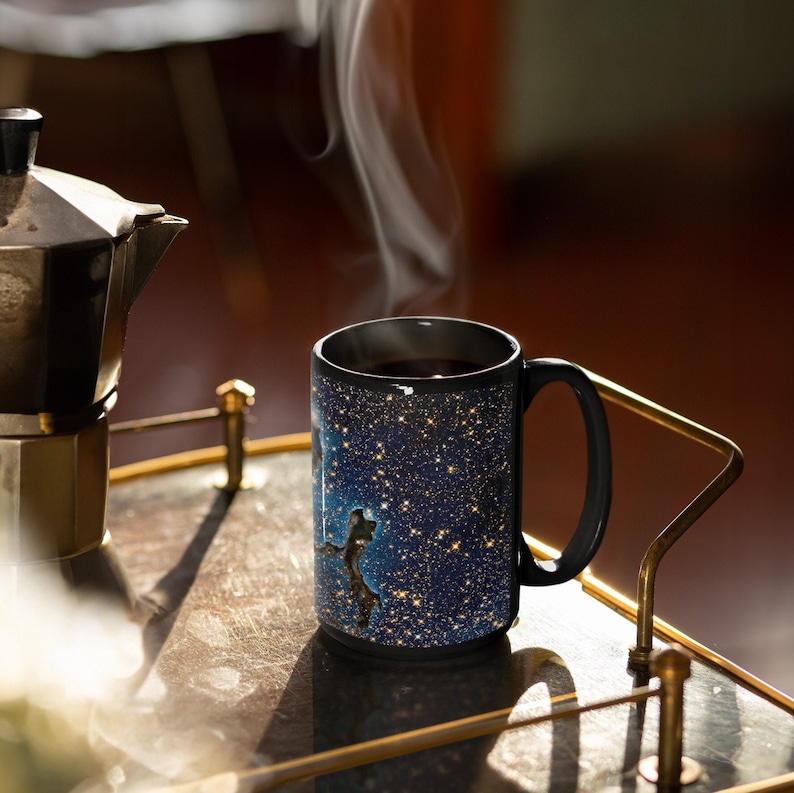 May include: A black coffee mug with a galaxy print design. The mug is filled with coffee and steam is rising from the top. The mug is sitting on a gold metal tray.