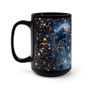 May include: Black ceramic mug with a colorful image of a nebula in space. The nebula is a swirling cloud of gas and dust, with a bright blue and white center. The background is a dark blue with many stars.