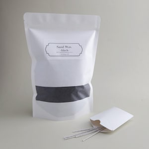 May include: A white pouch labeled "Sand Wax -black-" with a black band across the middle. A small white envelope contains several thin, gray sticks. The product is handmade in the USA.
