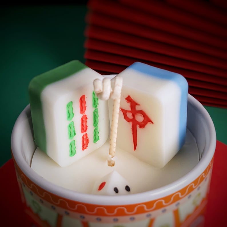 May include: A white ceramic candle holder with a red and green design. Two white ceramic mahjong tiles are placed inside the holder. One tile has a green and red design and the other has a red Chinese character.