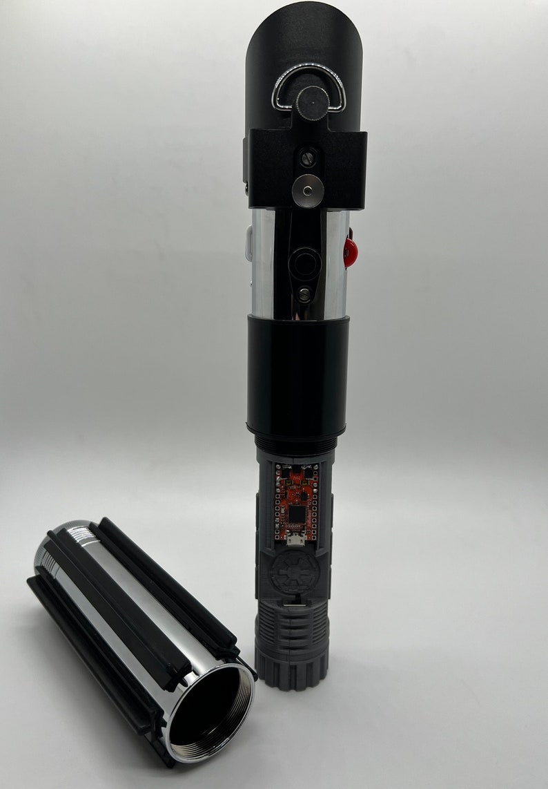 May include: A disassembled lightsaber with a black handle, silver blade, and a circuit board visible inside. The lightsaber is in two pieces, with the handle and blade separated.