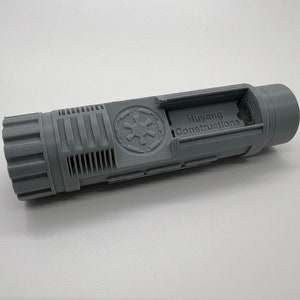 May include: A gray plastic model of a Star Wars blaster with the Imperial logo and the text "Huyang Constructions" printed on the side.