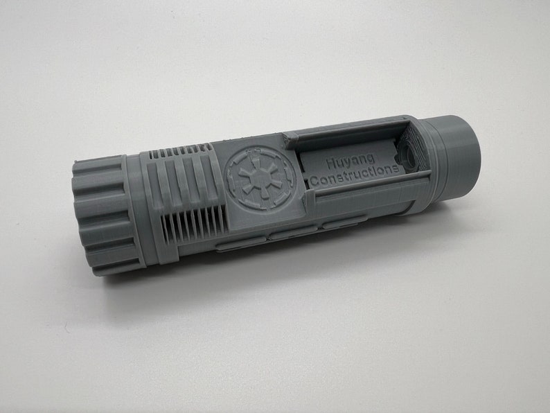 May include: A gray plastic model of a Star Wars blaster with the Imperial logo and the text "Huyang Constructions" printed on the side.