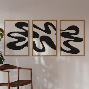 May include: Three framed abstract art prints with black and white abstract shapes on a white background. The frames are a light wood colour.