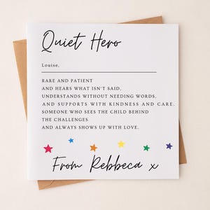 以下が含まれることがあります： 「Quiet Hero」の文字が黒い筆記体で書かれた白いグリーティングカード。カードにはメッセージが書かれており、カラフルな星で飾られています。カードは茶色の封筒に入っています。