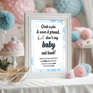 Puede incluir: Un cartel enmarcado en blanco con copos de nieve azules y blancos sobre un fondo azul. El cartel dice "Grab a pin & wear it proud. but don't say baby out loud! When you hear someone say baby take their pin. Whoever has the most in the end will win."