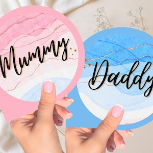 Op de afbeelding: Twee ronde borden met aquarel achtergronden en gouden glitter accenten. Het roze bord zegt "Mummy" en het blauwe bord zegt "Daddy".