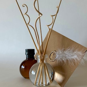 May include: A clear glass diffuser bottle with brown wooden sticks and a brown bottle of essential oil. The diffuser bottle is sitting on a brown envelope with a white feather and a wax seal.