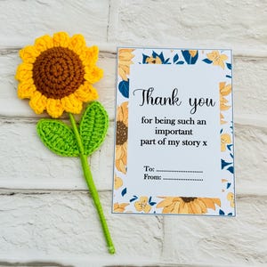 May include: A crocheted sunflower with yellow petals and a brown centre, green leaves and stem. A card with the text "Thank you" and space to write "To" and "From" is next to the sunflower.