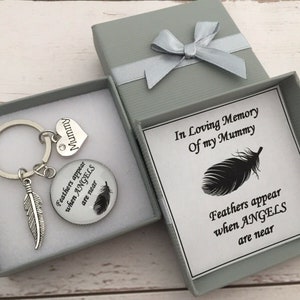 May include: A silver keyring with a feather charm and a round charm that says "Feathers appear when angels are near". The keyring is in a grey gift box with a white card that says "In loving memory of my mummy" and "Feathers appear when angels are near".