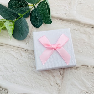 May include: A small white gift box with a pink satin ribbon tied in a bow.