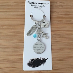 May include: A silver keyring with a feather charm, a small angel charm, a blue crystal charm, and a heart charm engraved with the word "Nana". The keyring also has a round tag with the text "Feathers appear when Angels are near".