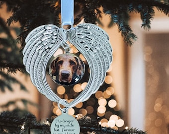 May include: Silver Christmas ornament with a photo of a brown dog in a round frame. The ornament has angel wings and a tag that reads "No longer by my side but Forever in my Heart" with a paw print.