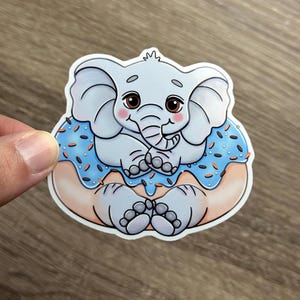 May include: A cute cartoon elephant wearing a blue and white donut with sprinkles. The elephant is sitting on the donut and has a happy expression on its face.