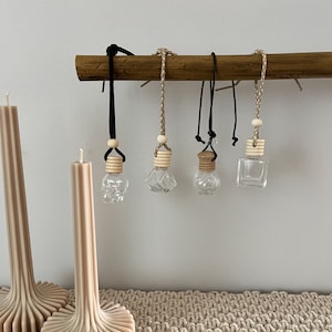 May include: Five glass bottles with wooden caps and black cords hanging from a wooden dowel. The bottles are empty and clear. The bottles are hanging from a wooden dowel.