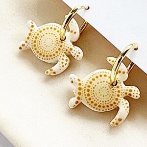 May include: A pair of gold hoop earrings with white turtle charms. The turtles have a gold dot pattern.