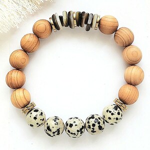 May include: A bracelet made with natural wood beads and dalmatian jasper beads. The bracelet has gold spacers and a centre piece of brown and white shell.