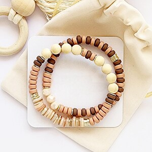 May include: Two beaded bracelets with brown, beige and cream coloured beads. The bracelets are stacked on top of each other and are on a white background.