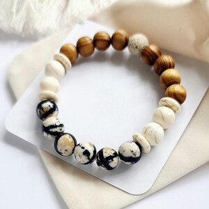 May include: A bracelet made of brown, white and black beads. The beads are arranged in a pattern of brown, white and black. The bracelet is on a white surface.