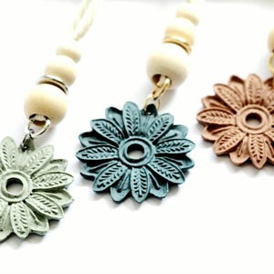 May include: Three wooden bead necklaces with decorative flower charms. The flowers are teal, green, and brown.