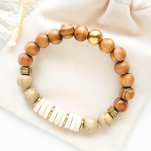 May include: A wooden beaded bracelet with gold accents and white beads. The bracelet is on a white background.