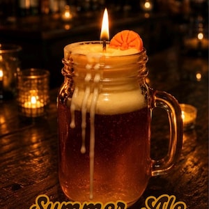 May include: A beer-shaped candle in a glass mason jar mug with a handle. The candle features a lit wick, a white foam top with wax drips running down the side, and an orange slice garnish. Text reads That Dope Soap & Candle Co Summer Ale Mini Beer Candle.