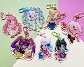 Op de afbeelding: Een verzameling van zeven acryl sleutelhangers met diverse anime-stijl personages met levendige haarkleuren en outfits. Elke bedel bevat een kleurrijke plastic karabijnhaak. De ontwerpen tonen figuren met roze, blauwe, blonde en groene haaraccenten.
