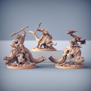 May include: Three miniature figurines of lizard-like creatures riding on the backs of larger lizard-like creatures. The figures are painted in a light brown color and are posed in a dynamic fashion.