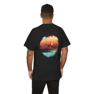 May include: Black t-shirt featuring a circular graphic of a sunset over a pier. The graphic is in shades of red, orange, yellow, blue, and green.
