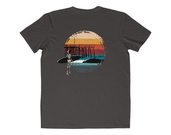 May include: A dark gray t-shirt with a vintage-style graphic of a skeleton surfing in front of a pier. The graphic is in a circle with a sunset background.