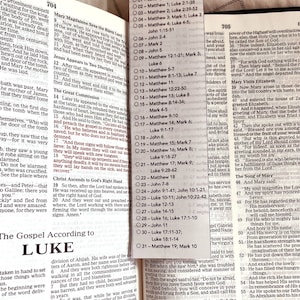 May include: Open Bible with text from the Gospel According to Luke. A clear, rectangular bookmark with the word "October" and a list of Bible readings is placed on the page.